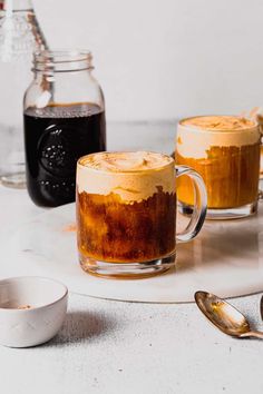 two mugs filled with liquid sitting on top of a table next to spoons