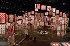 people are standing in the middle of a room with red and white quilts hanging from the ceiling