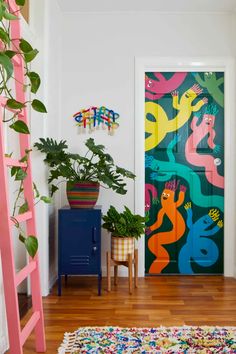 a brightly colored door in a white room with pink ladders and potted plants