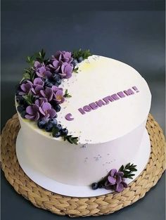 there is a white cake with purple flowers on the top and letters painted on it