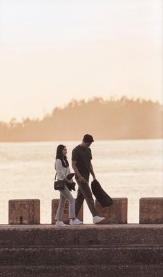 two people walking along the edge of a body of water with their bags in hand