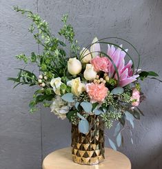 a vase filled with lots of flowers on top of a wooden table next to a wall