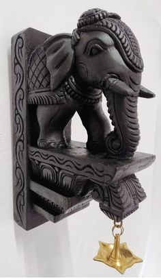 an elephant statue on a shelf with a bell hanging from it's back end