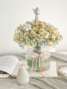 a vase filled with white and yellow flowers on top of a table next to an open book