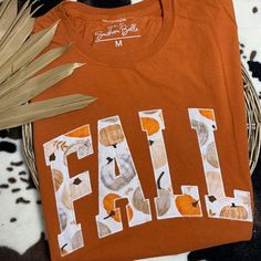 an orange shirt with the word fall printed on it next to some plants and leaves