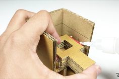 a hand is holding an open cardboard box with a house in it and glue on the inside