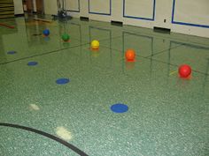 an indoor gym with balls on the floor and blue circles painted on the floor around them