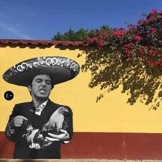 a man wearing a sombrero and holding a chicken in front of a yellow wall