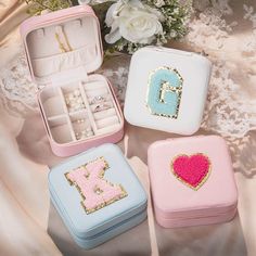 three small jewelry boxes with designs on them and flowers in the background, one is pink, one is blue