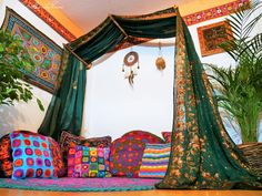 a bed covered in lots of pillows next to a potted plant and wall hangings