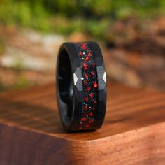 a ring with red and black stones inlayed to it on a wooden surface