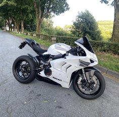 a white motorcycle parked on the side of a road next to some grass and trees