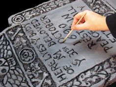 a person holding a brush and writing on a large piece of metal with ornate designs