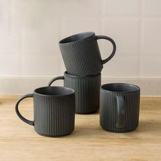 three black mugs sitting on top of a wooden table