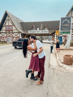 a man and woman kissing on the street in front of a building with a sign