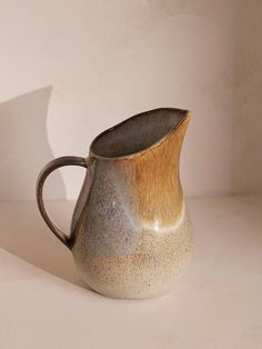 a brown and white vase sitting on top of a table next to a wall with a shadow cast on it