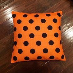 an orange and black polka dot pillow sitting on top of a wooden floor next to a coffee table