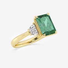 an emerald and diamond ring with two diamonds on the side, set in yellow gold