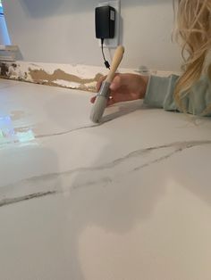 a woman using a paint roller on a white surface