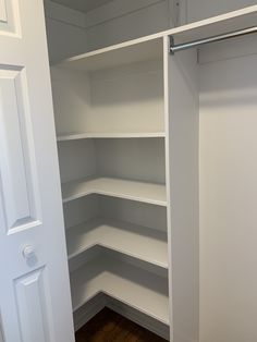 an empty walk in closet with white shelving and wood flooring on the side