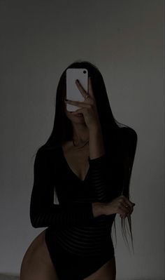 a woman in a black bodysuit taking a selfie with her cell phone while sitting on a bed