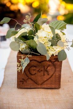 a wooden box with flowers and greenery in it sitting on a burlap table