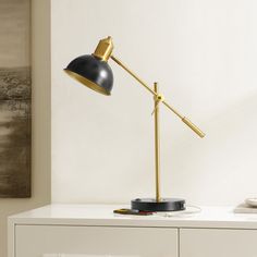 a black and gold desk lamp sitting on top of a white dresser next to a painting