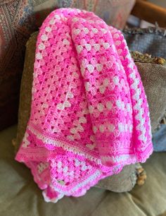 a pink and white crocheted blanket sitting on top of a couch next to a pillow