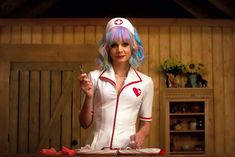 a woman with pink and blue hair standing in front of a table holding a fork