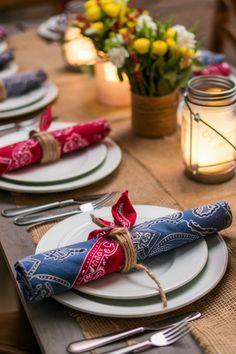 the table is set with place settings, napkins and flowers in mason jar vases