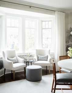 a living room with two white chairs and a round table in front of three windows