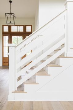 a white stair case in a house with wood floors and doors on both sides, leading to the second floor