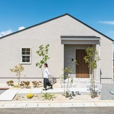 a man walking past a small house with a tree in front