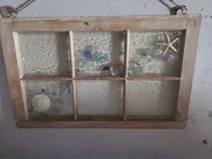 an old window with sea glass and starfish on the inside is hanging from a rope