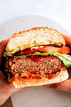 a hand holding a sandwich with meat, lettuce and tomato