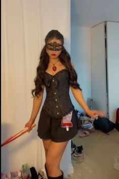 a woman in a black dress and mask holding a red bat while standing next to a white wall