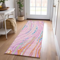 a pink and orange rug on the floor in front of a door with a potted plant