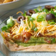 an enchilada is topped with cheese, lettuce and olives