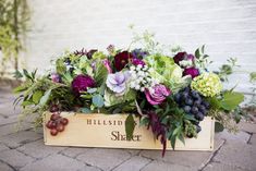 a wooden box filled with lots of flowers and greenery next to a brick wall