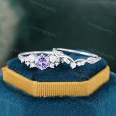 a ring with an amethorate and white diamonds on it, sitting on top of a blue velvet cushion