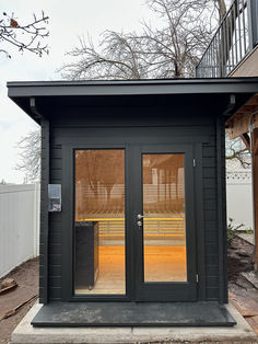 a small black building with two doors on each side and a balcony above the door