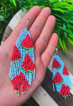 a hand holding a pair of red and blue beaded earrings with watermelon designs