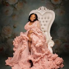 a woman in a pink dress is sitting on a white chair with flowers behind her