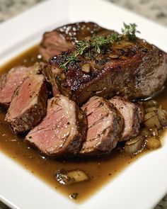 a white plate topped with meat covered in sauce and garnished with green sprigs