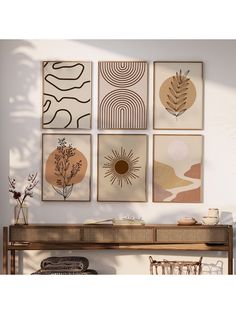 four framed art pieces hang on the wall above a wooden table with a plant and vase