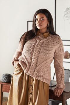 a woman standing in front of a wooden table wearing a sweater and skirt with buttons