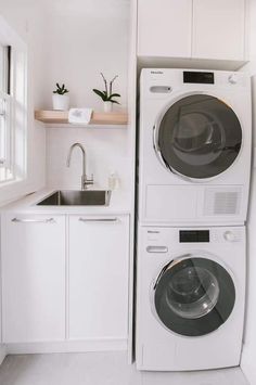 a washer and dryer in a white kitchen with wooden shelves on the wall