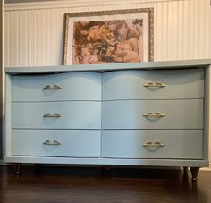 a blue dresser with gold handles in a room next to a painting on the wall