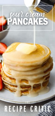 pancakes with syrup being drizzled on top and strawberries in the background