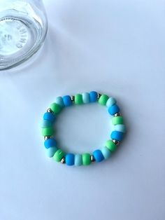 a blue and green beaded bracelet next to a glass